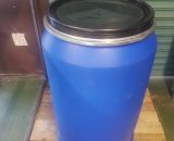 A blue plastic barrel with a black lid standing on a wooden pallet.