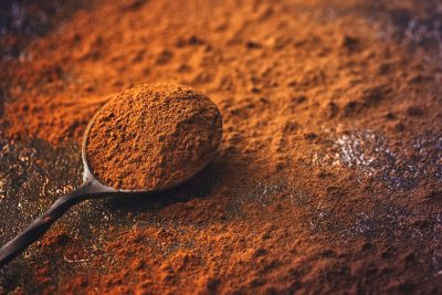 A spoonful of ground spice on a textured surface, with spilled spice powder scattered around it.