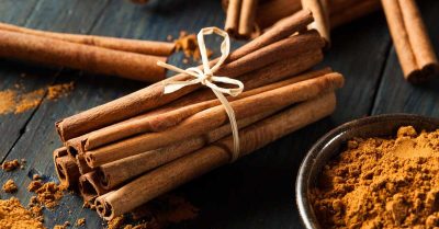 A bundle of cinnamon sticks tied with a string next to a small bowl of ground cinnamon on a dark wooden surface.