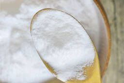 A close-up image of a spoonful of white powdered substance, possibly sugar or flour, against a blurred background.